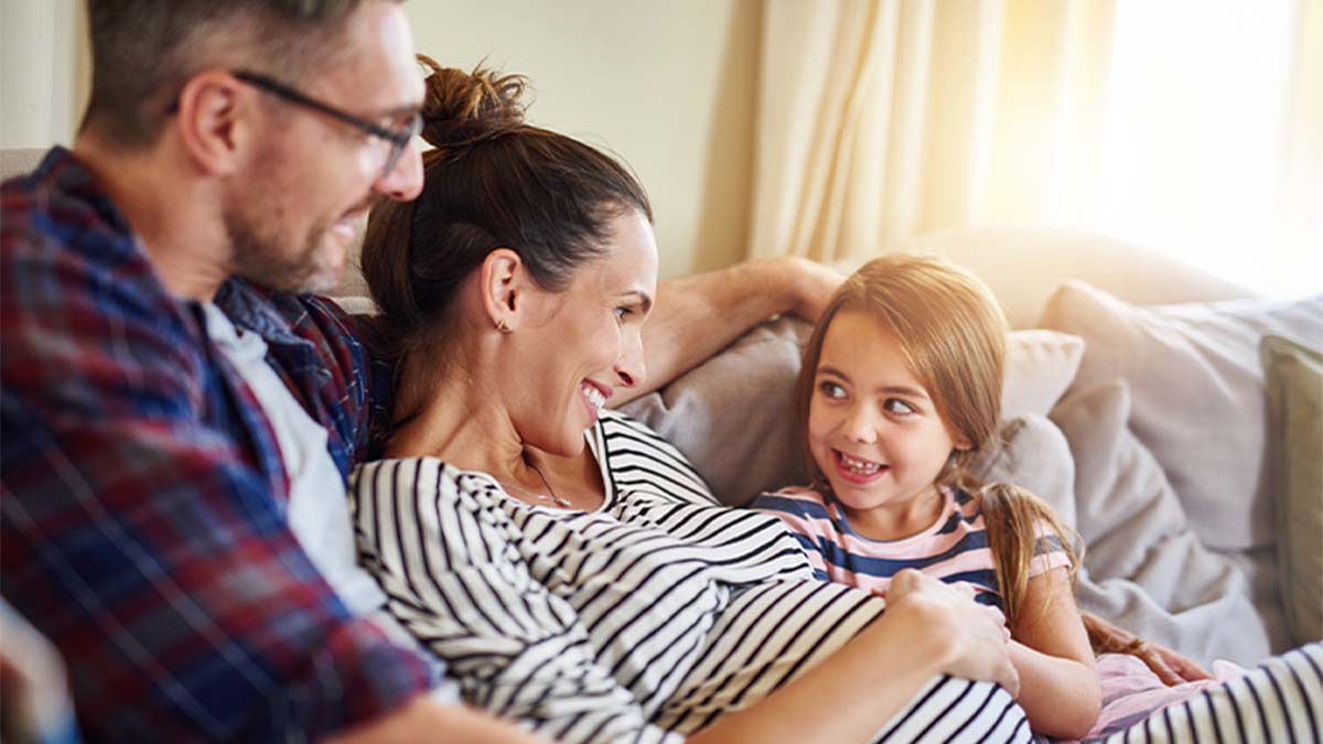 Pai, mãe e filha pequena sentados num sofá